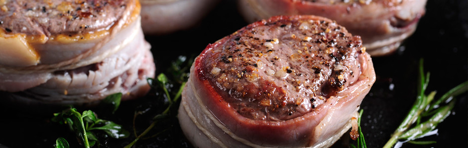 Mit Schinkenstreifen ummantelte Wildfilets-Medaillons in dunkler Pfanne mit Rosmarinzweigen garniert